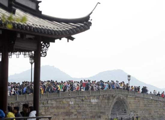4月6日，游客走在西湖断桥上。当日是清明小长假第二天，众多市民和外地游客“扎堆”涌入杭州西湖景区游玩，景区内人头攒动。 新华社记者 韩传号 摄