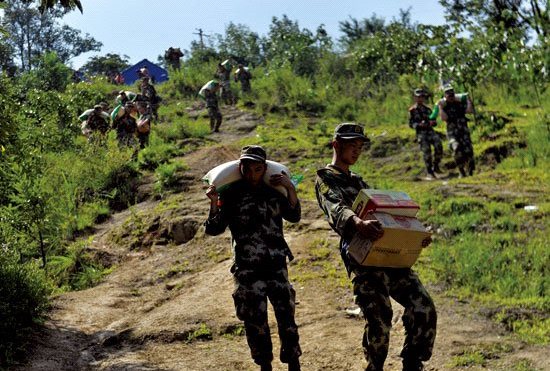 救援官兵从山顶搬运救灾物资，沿着陡峭的山坡往下赶。黄漩 摄