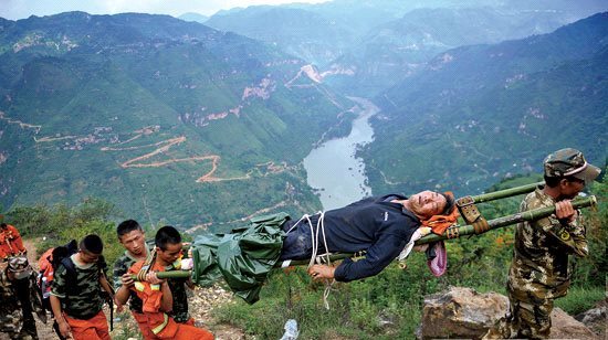 75岁老人代时林地震时受伤，救援人员用自制担架将老人从山脚抬向山顶。
