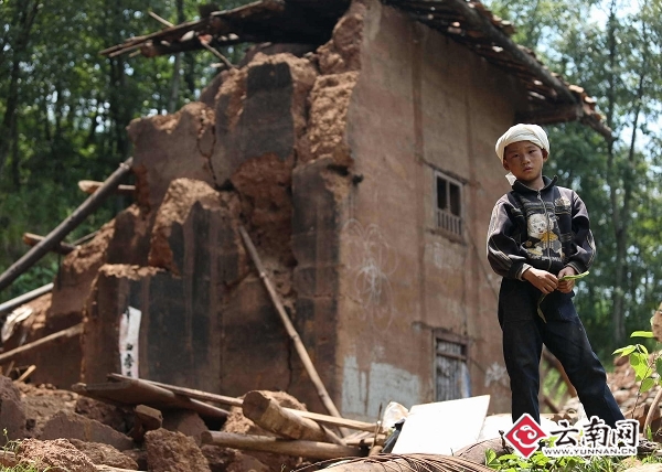 光明村,12岁的小孩站在自家倒塌的房前,他的家人在地震中丧生。