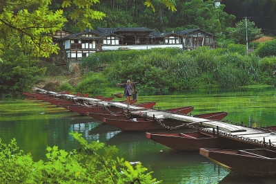 老人挑着农具走过浮桥。他身后的房屋，是著名记者、革命烈士羊枣的居住旧址，现为国家级文物保护单位。