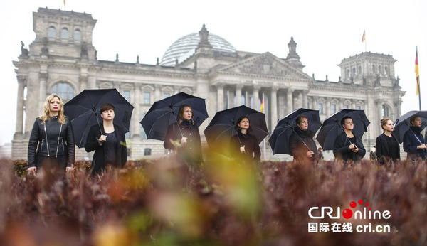 当地时间2014年10月18日,德国柏林,女活动家身穿黑衣,手举雨伞在国会大厦前游行,抗议人口贩卖。图片来源:CFP