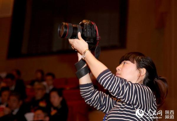 届人民代表大会第三次会议开幕现场,一名女记者为了能够拍摄到主席台