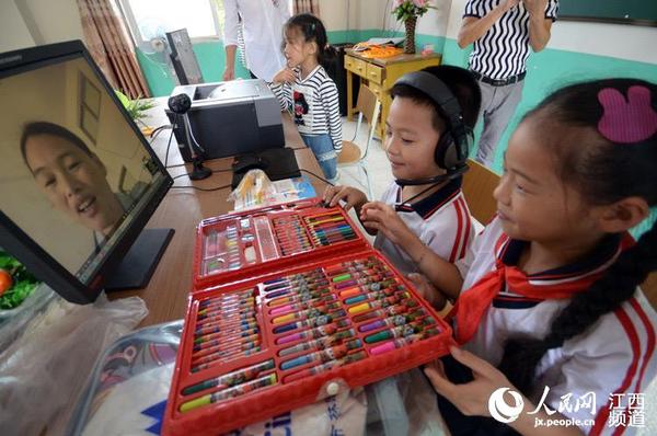 在学校的视频教室中,孩子们拿着刚刚分发到的礼物给镜头里的父母看。