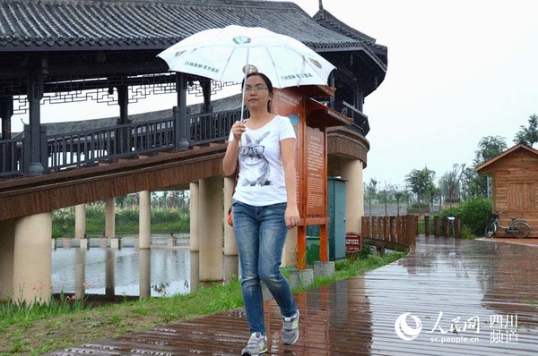 一位市民打着雨伞走过东坡城市湿地公园内的观景楼。（刘浏 摄）
