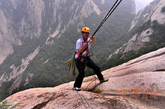 身系绳索的环卫工在悬崖上工作十分危险。