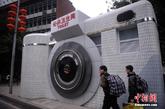 2月6日，重庆市民正经过“照相机”公厕。创意“照相机”厕所亮相重庆石桥铺数码城，以“照相机”外形来修建的公共卫生间，成为一道创意城市风景线。图为市民正经过“照相机”公厕。实习编辑：李黎星）
