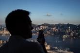 2014年8月23日，中国香港，一男子正在用手机拍摄香港维多利亚港口美景。眺望香港尖沙咀海运码头、香港海运大厦，香港中银大厦 BOC Tower，香港国际金融中心IFC、香港维多利亚港。