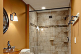 以橘黄色墙面为主色调的卫浴空间里，淋浴区则以大块面砖墙造型呈现，并塑造出了这一空间整个墙面的层次感，简约的玻璃移门来作为空间隔断，实用且美观。墙面上的壁灯使这一空间中有股淡淡的复古感觉。
