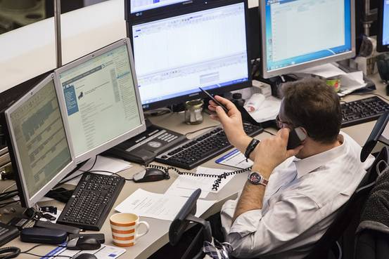 一名金融交易员一边打电话一边关注着电脑屏幕上的数据.